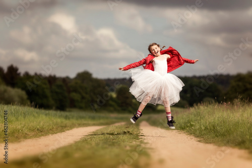 Portrait of happy girl wearing red leather jacket and tutu jumping in the air on dirt track photo