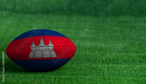 American football ball  with Cambodia flag on green grass background  close up