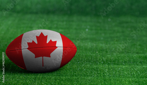 American football ball  with Canada flag on green grass background, close up photo