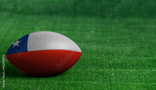 American football ball with Chile flag on green grass background, close up