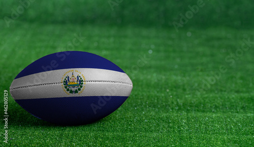 American football ball with El Salvador flag on green grass background, close up