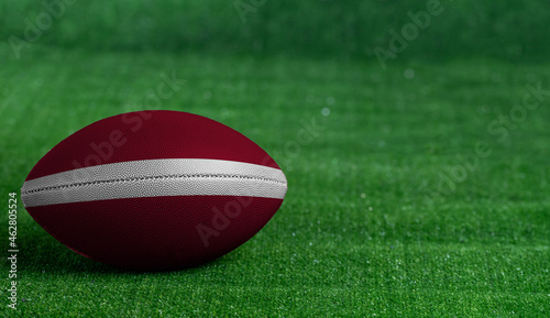 American football ball with Latvia flag on green grass background, close up