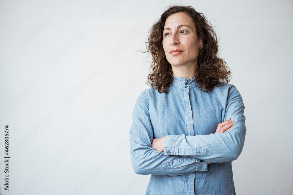 Thoughtful businesswoman with arms crossed standing against white wall Thoughtful businesswoman with arms crossed standing against white wall