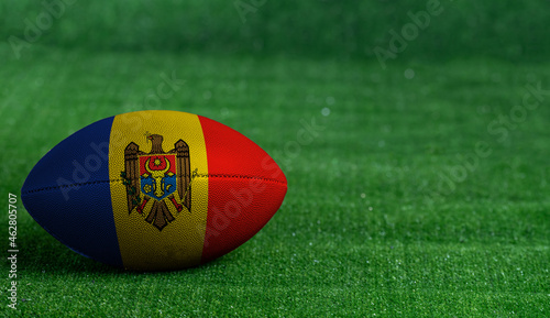 American football ball with Moldova flag on green grass background, close up
