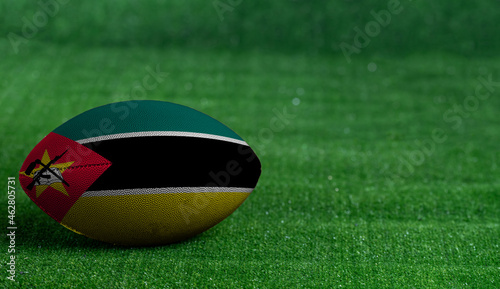American football ball  with Mozambique flag on green grass background  close up