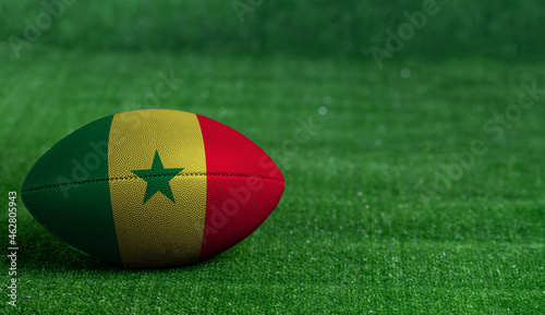 American football ball with Senegal flag on green grass background, close up