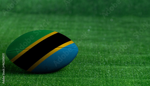 American football ball with Tanzania flag on green grass background, close up