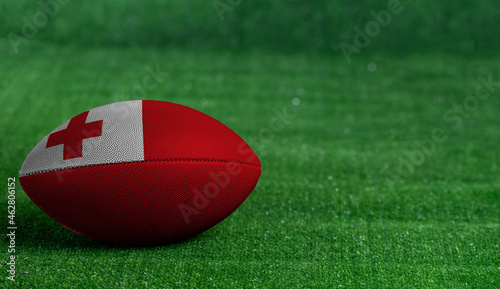 American football ball with Tonga flag on green grass background, close up