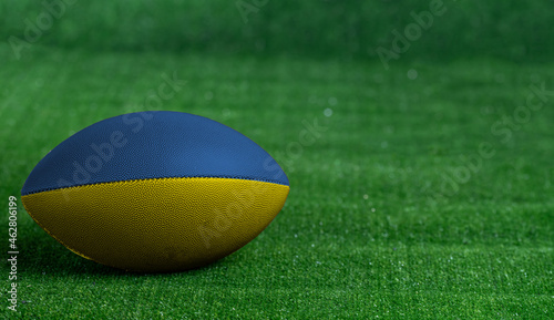 American football ball with Ukraine flag on green grass background, close up