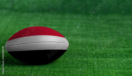 American football ball  with Yemen flag on green grass background  close up