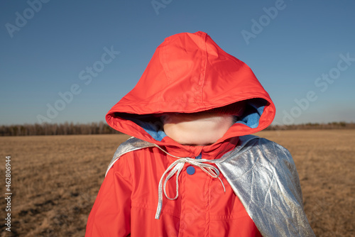 Boy dressed up as superhero in steppe landscape hiding his face in hood of his jacket photo