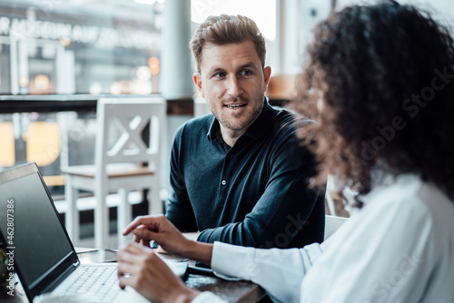 Businessman discussing with colleague using laptop while sitting at cafe photo