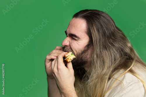 Bearded man eating sandwich in front of green background