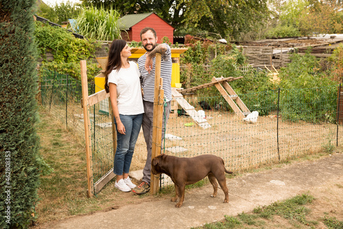Portrait of couple with dog standing at chickenhouse in garden photo
