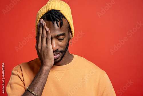 Portrait of stylish young man covering one eye in front of orange wall photo