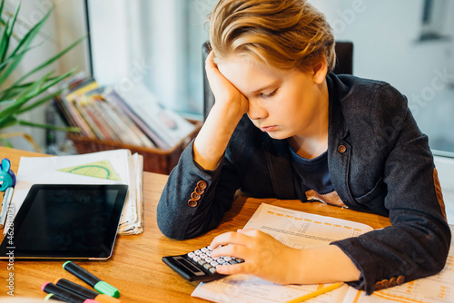 Frustrated boy sitting at desk with workbook and pocket calculator