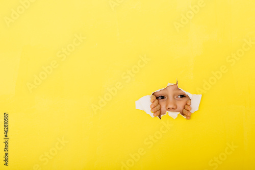 Close-up of curious boy tearing yellow paper for peeking photo