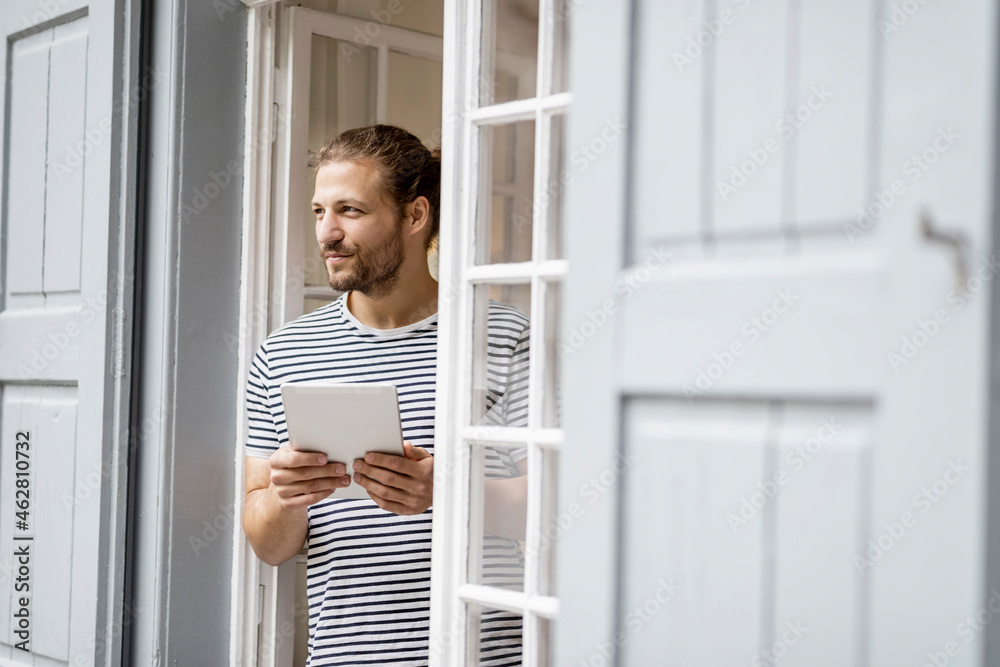 Young man with tablet standing at terrace door at home Young man with tablet standing at terrace door at home