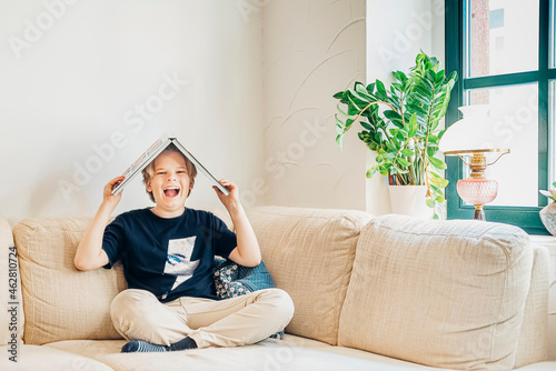Portrait of laughing boy sitting on couch in living room with a book