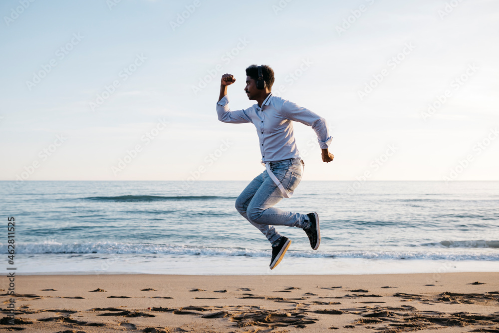 Mid adult man jumping at beach during sunny day Mid adult man jumping at beach during sunny day