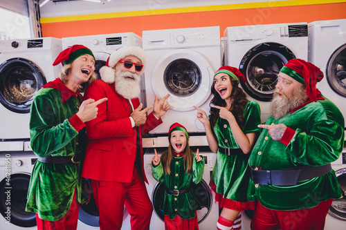 Portrait of attractive cheerful funky group elfs demonstrating domestic wash machine laundry eve advent offer at store market indoors