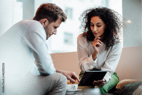Businesswoman working on digital tablet with colleague while sitting at cafe