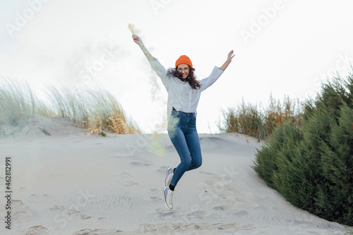 Happy young woman with smoke bomb jumping against sky photo