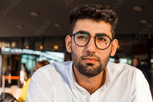 Portrait of pensive young businessman with beard and glasses at sidewalk cafe
