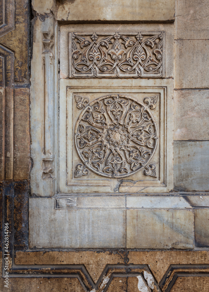 Round floral patterns framed by geometrical patterns carved into the exterior ancient stone wall of Sultan Hasan Mosque, Old Cairo, Egypt