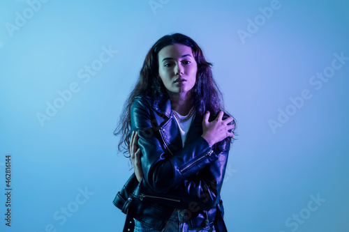 Confident teenage girl wearing leather jacket posing against blue background
