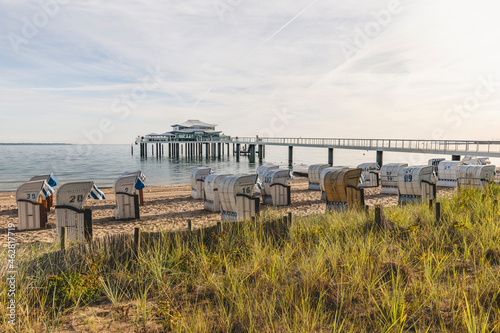 Germany, Schleswig-Holstein, Timmendorfer Strand, Hooded beach chairs on sandy coastal beach with teahouse at end of pier in background photo