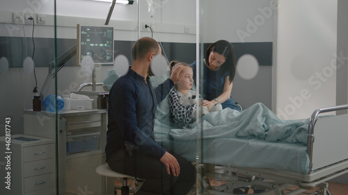 Sick daughter wearing oxygen nasal tube lying in bed after illness surgery waiting for medical examination with parents in hospital ward. Hospitalized child recovering after flu isickness nfection photo