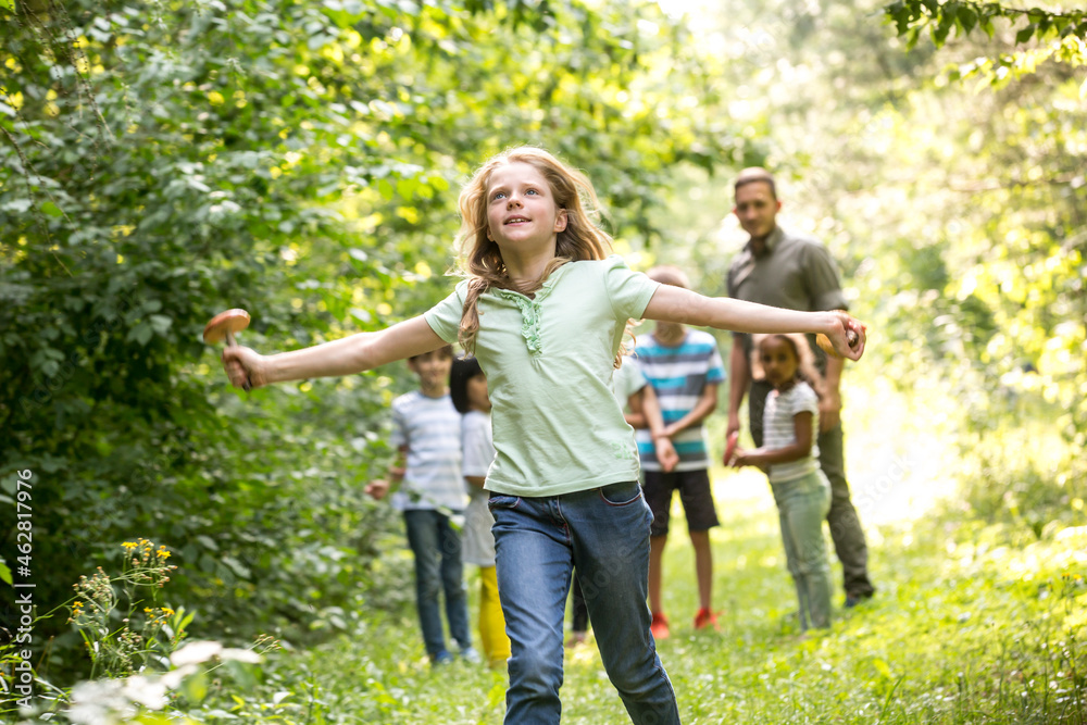 School children walking in forest with their teacher, girl running, holding mushroom School children walking in forest with their teacher, girl running, holding mushroom