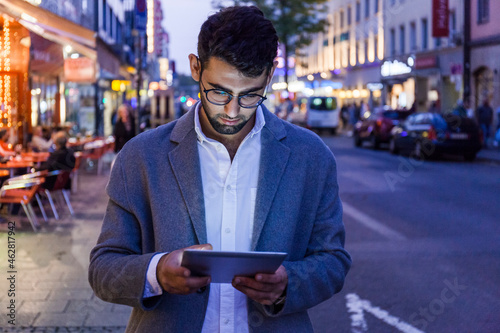 Germany, Munich, young businessman using digital tablet in the city at dusk photo