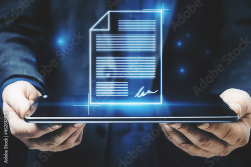 Close up of businessman hands holding tablet with abstract digital document hologram. Electronic signature and transformation concept.