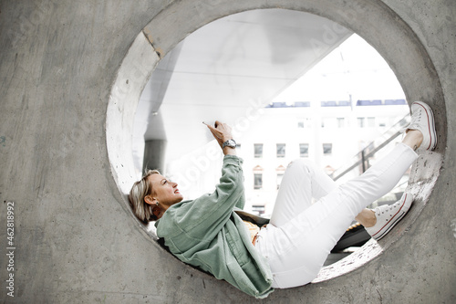 Full length of side view of mature woman using mobile phone while lying on concrete circle in wall