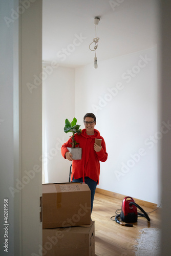 Young woman moving into her new home, carrying a potted plant photo