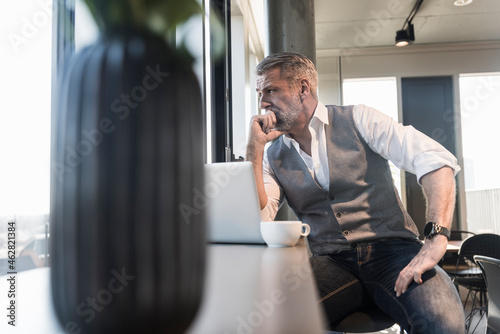 Serious mature businessman with laptop looking out of window