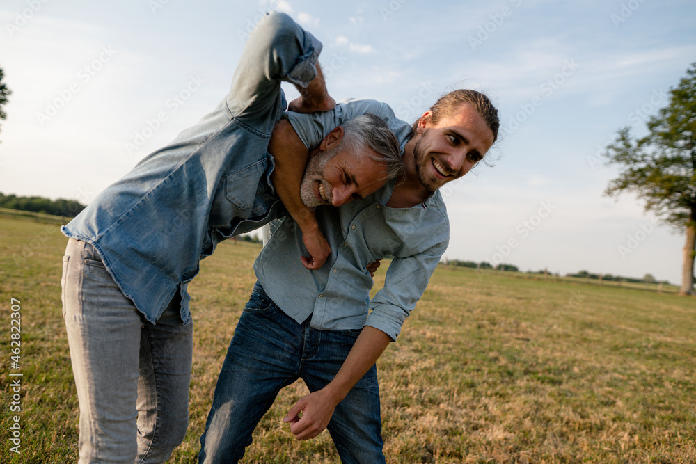 Happy father and adult son playfighting on a meadow in the countryside Happy father and adult son playfighting on a meadow in the countryside