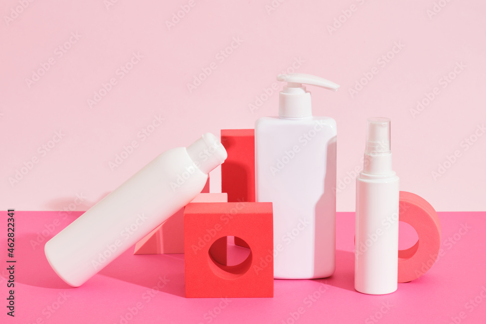 several different white plastic bottles and tube on pink geometric podiums on pink background several different white plastic bottles and tube on pink geometric podiums on pink background