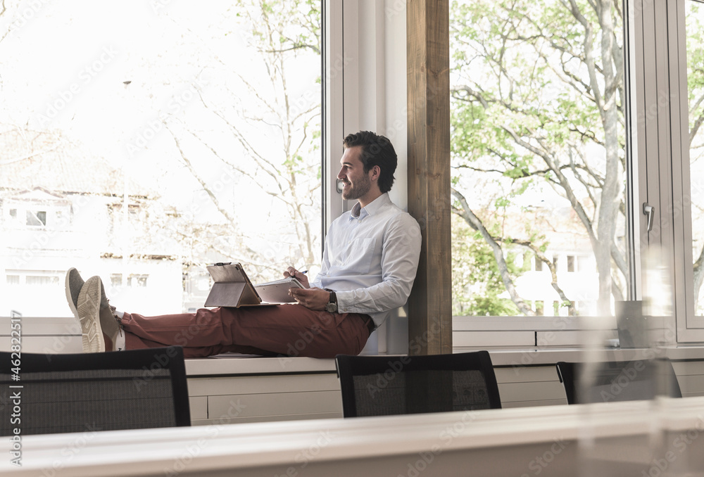 Young businessman sitting on windowsill, using digital tablet