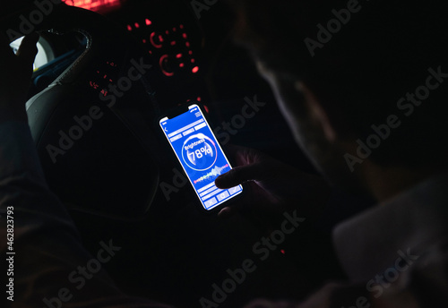 Close-up of young man adjusting brightness of cell phone in car at night