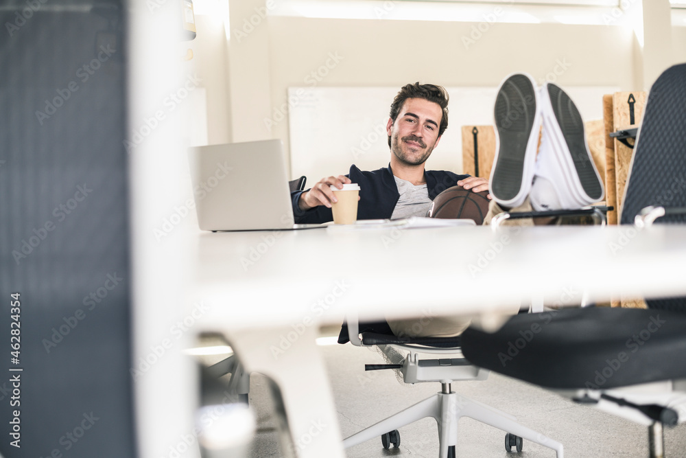 Young businessman sitting in office, with feet on desk, drinking coffee Young businessman sitting in office, with feet on desk, drinking coffee