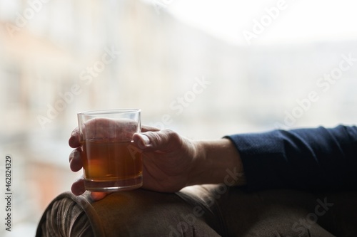 Close up shot of hand of successful business man holding glass of alcohol scotch whiskey while relaxing in a chair