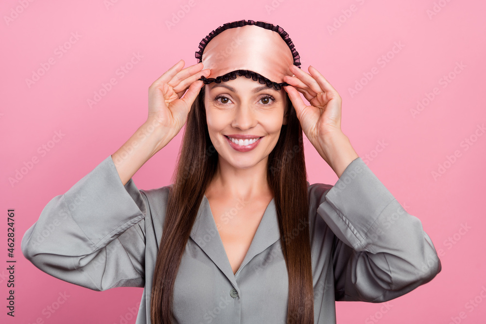 Photo of mature woman happy positive smile hand touch eye mask night isolated over pink color background Photo of mature woman happy positive smile hand touch eye mask night isolated over pink color background