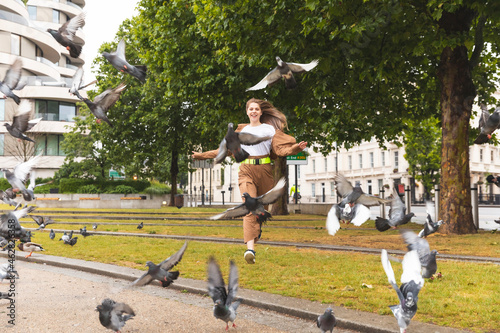 Carefree young woman having fun at park and chasing pigeons, London, UK