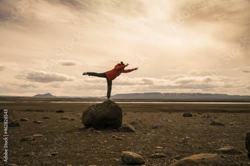 Young woman balancing on one leg on a rock in the volcanic highlands of Iceland