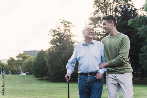 Young man assisting his grandfather walking in a park photo