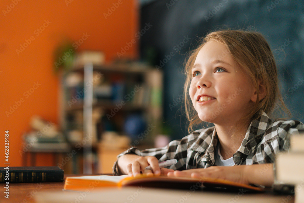 Close-up view of adorable pupil school girl kid listening to teacher sitting sitting at table with paper book in classroom. Portrait of elementary child schoolgirl studying at home, selective focus. Close-up view of adorable pupil school girl kid listening to teacher sitting sitting at table with paper book in classroom. Portrait of elementary child schoolgirl studying at home, selective focus.