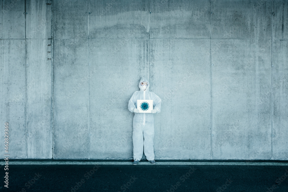 Man wearing protective clothing holding sign with a depiction of a virus Man wearing protective clothing holding sign with a depiction of a virus